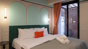 Een opgemaakt bed met wit en oranje beddengoed, een groen bekleden hoofdeinde, en een stapel opgerolde handdoeken aan de zijkant.