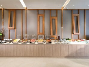 Un buffet composé de différents plats présentés dans des récipients en verre, un mur recouvert de panneaux en bois et un sol carrelé.