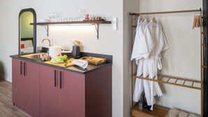 Een kitchenette met een spoelbak, een snijplank en diverse keukenbenodigdheden. Er is een houten rek met handdoeken en een houten kast met lades.