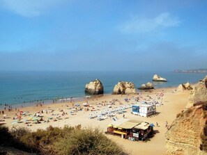 A beach with rocky formations, a sandy shore, and a small building with a roof. - Morley Apartment, Praia da Rocha, Algarve (Portimão)
