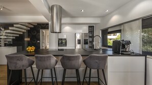 A modern kitchen with a central island, bar stools, stainless steel appliances, and a large window.