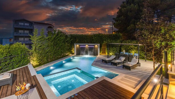 A rooftop pool area with a waterfall feature, lounge chairs, and a wooden deck.