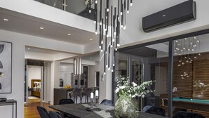 A modern dining area with a marble table, black chairs, a vase with flowers, and a pool table in the background.