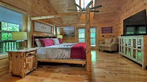 Une chambre dans une cabane en bois, avec un lit, une petite table, un placard et un ventilateur de plafond.