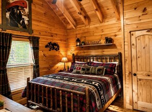 A wooden cabin bedroom with a bed, a window with curtains, a wall-mounted shelf with a bear decoration, and a door. - Pet-friendy, lake-front cabin rental with outdoor fireplace, dock w/Jon Boat (Ellijay)