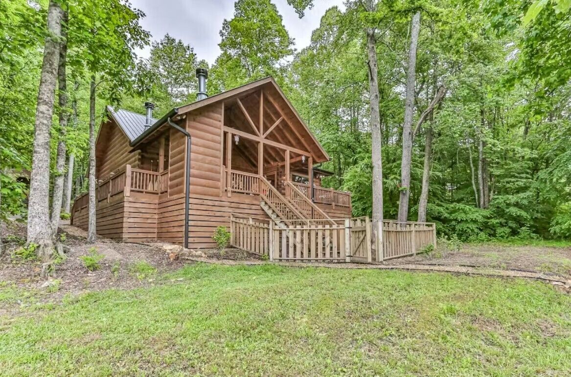 Une cabane en bois dotée d’un porche et d’un escalier, entourée d’arbres.
