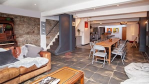A spacious living area with a stone wall, a wooden staircase, a dining table with chairs, and a kitchen in the background. - higgihaus 5 5 of 7 Rooms Monday - Friday (Cardiff)