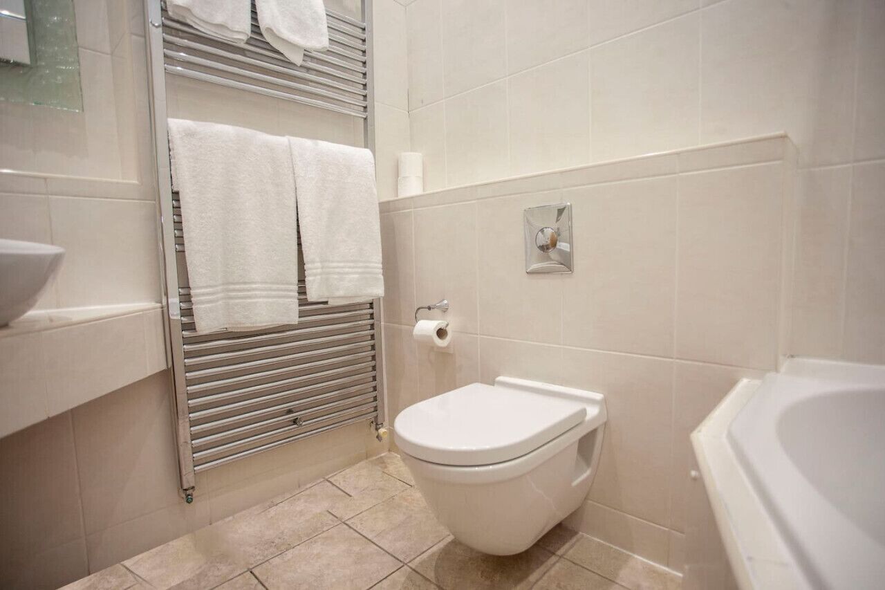 Un baño con inodoro, toallero con dos toallas, dispensador de papel higiénico y bañera.