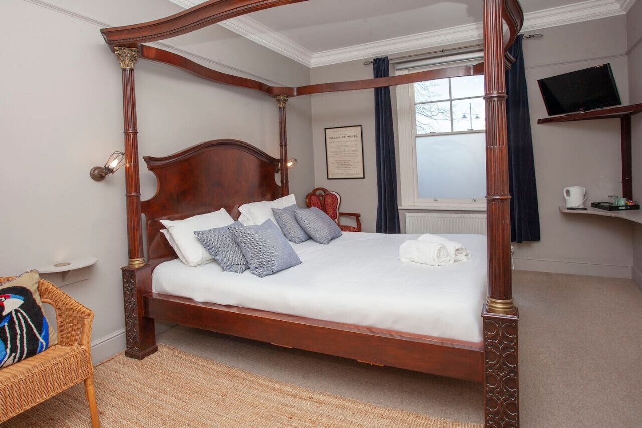 A four-poster bed with a wooden frame, white bedding, and multiple pillows.
