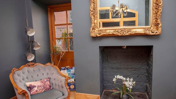 A room with a fireplace, a large mirror, a tufted armchair, and a wall-mounted lamp. - higgihaus 5 5 of 7 Rooms Monday - Friday (Cardiff)