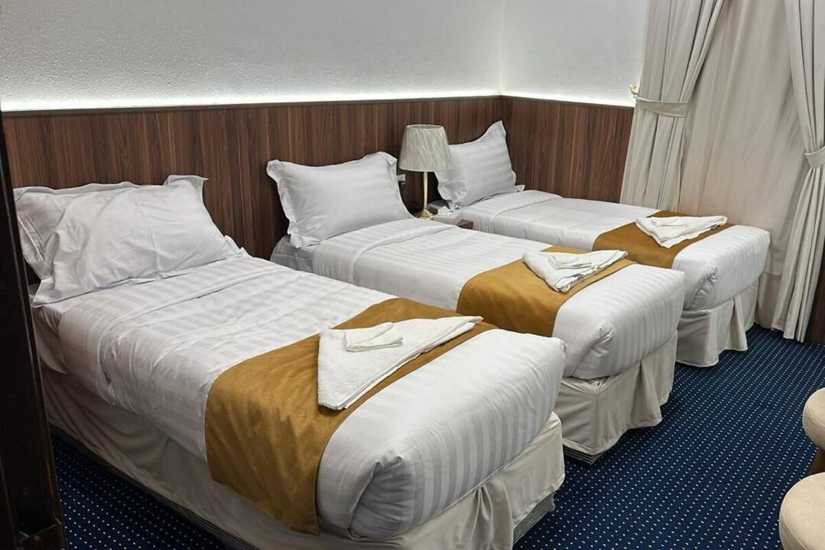 A hotel room with two single beds, a small table, a chair, and a refrigerator.