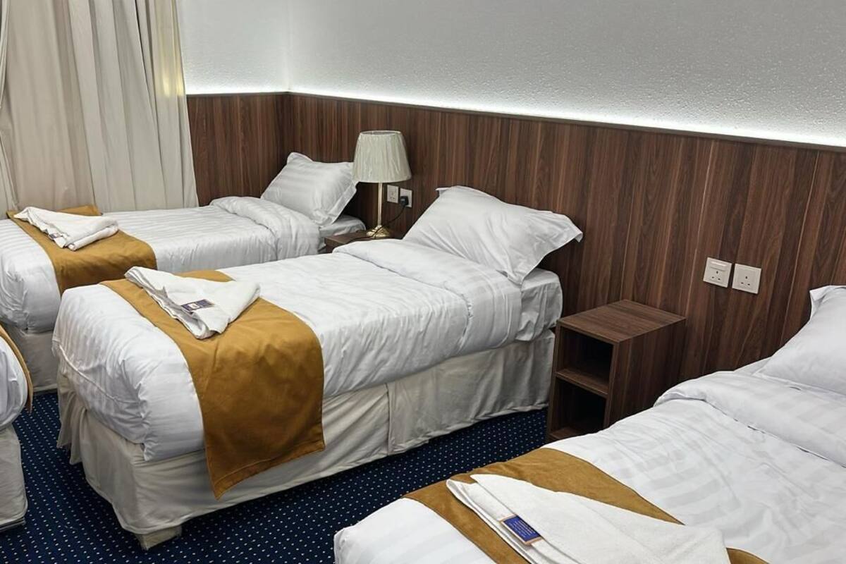 A hotel room with two single beds, a small bedside table, a lamp, and a curtain.