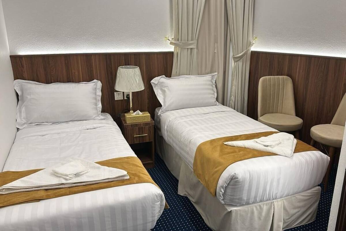 A hotel room with two beds, a nightstand, a lamp, a chair, and a curtain.