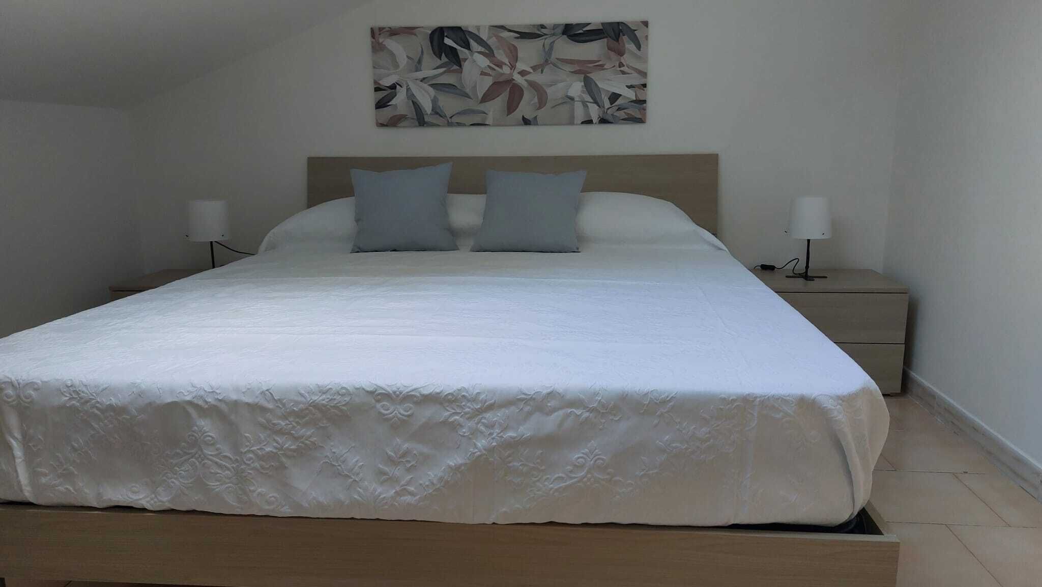 Een opgemaakt bed met een houten hoofdeinde en twee bedlampjes.