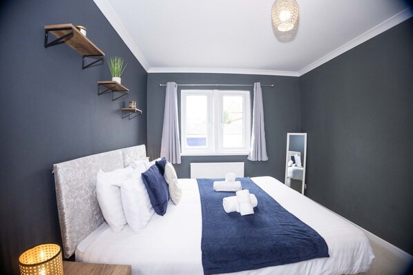 A modern bedroom with a large bed, bedside tables, a window with curtains, and a bedside lamp.