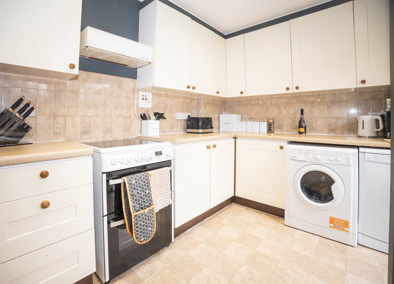A kitchen with white cabinets, a stove, a microwave, a washing machine, and a coffee maker.