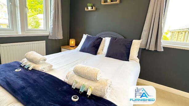A bedroom with a bed, bedside tables, a nightstand, a window with curtains, and a view of greenery outside. - Large House | Convention Centre | 20% Discount (Harrogate)