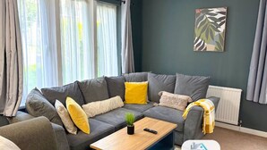 A modern living room with a grey sectional sofa, a wooden coffee table, and a plant. - Large House | Convention Centre | 20% Discount (Harrogate)