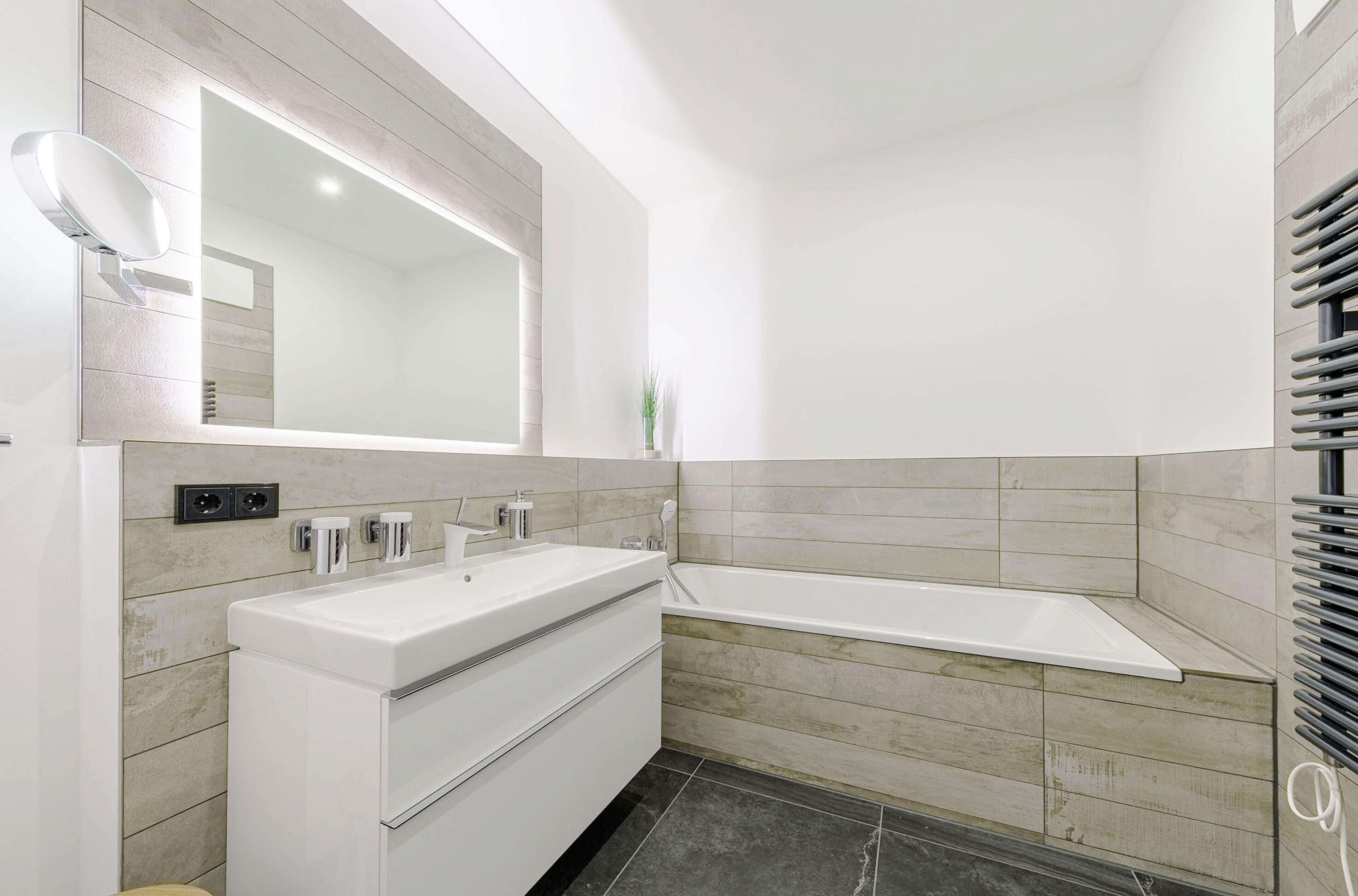 Une salle de bain moderne avec un meuble-lavabo blanc, un grand miroir et une baignoire d’angle.