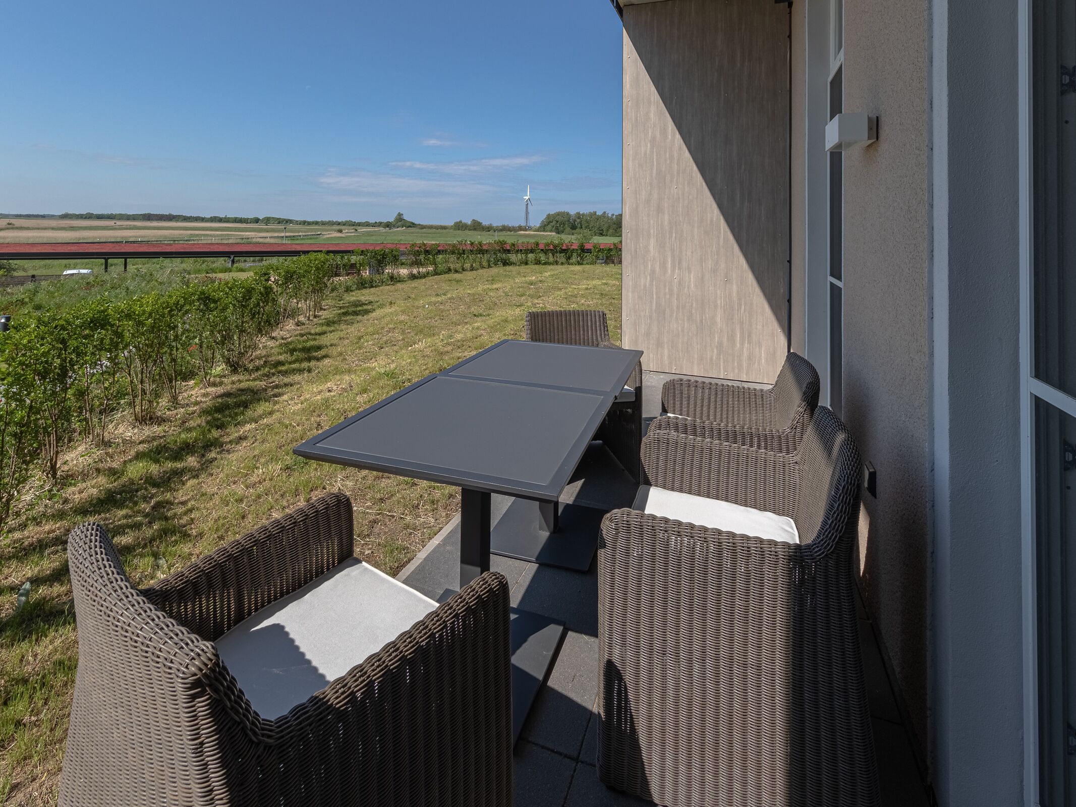 Un patio al aire libre con una mesa y sillas de mimbre, con vistas a un viñedo y un cielo despejado.