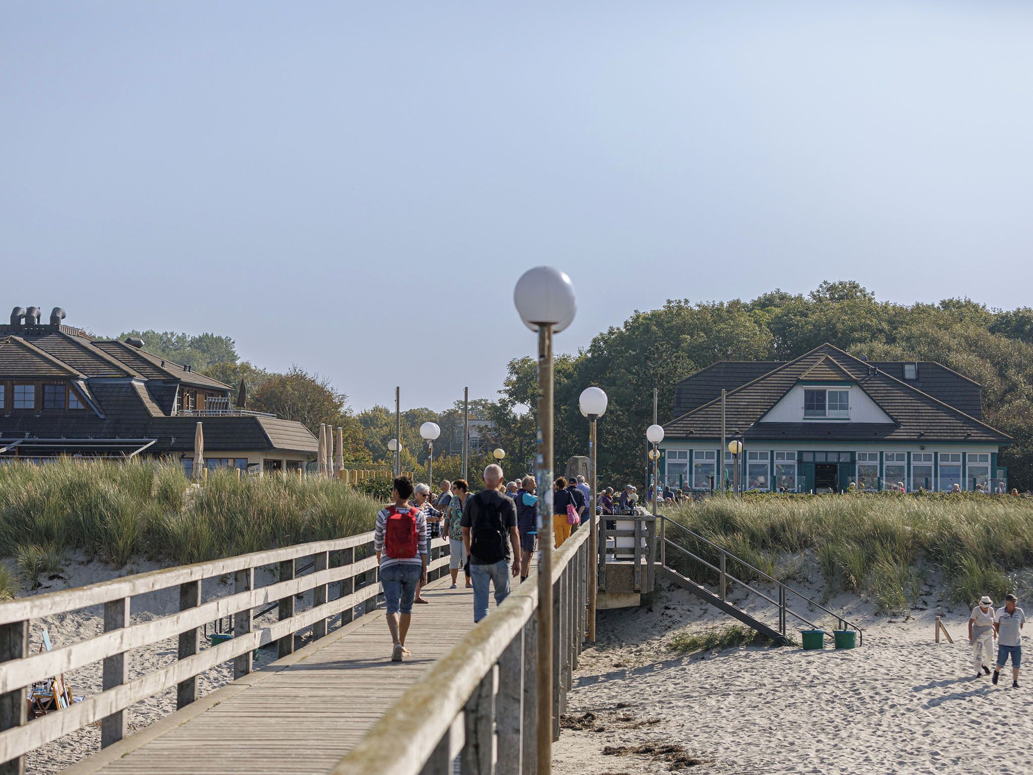 Une promenade en bois mène à une plage, avec des bâtiments visibles en arrière-plan.