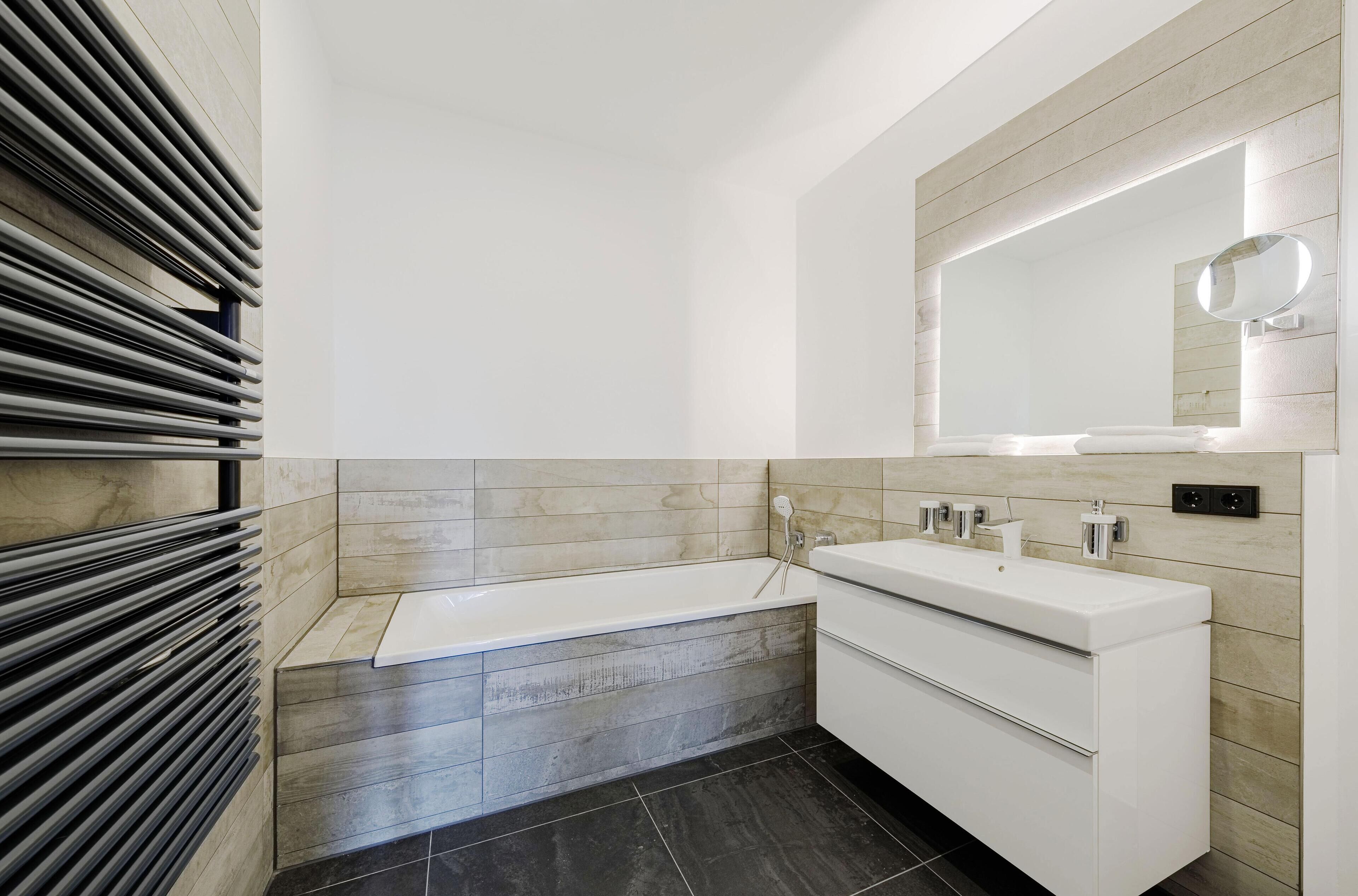 A modern bathroom with a bathtub, a vanity with a mirror, and a towel rack.