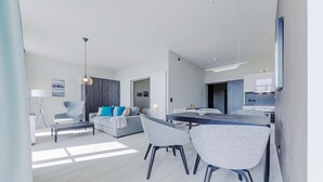Ein modernes Wohnzimmer mit einer Couch, einem Esstisch mit Stühlen und einer Küchenzeile im Hintergrund.
