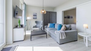 Ein modernes Wohnzimmer mit grauem Sofa, einem Couchtisch, einem an der Wand montierten Fernseher und einer Pendelleuchte.