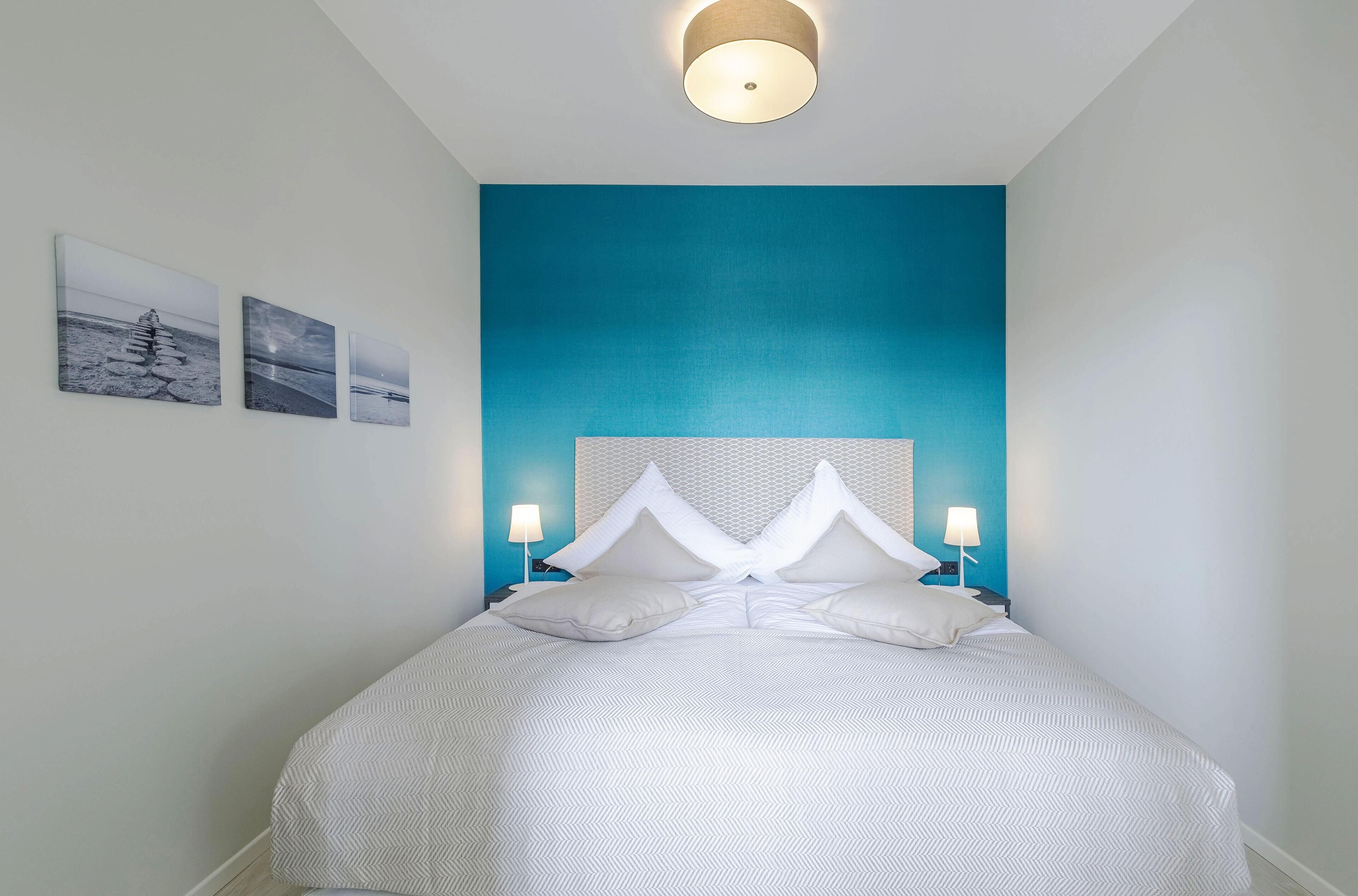 Un dormitorio moderno con una cama grande, un cabecero azul y tres cuadros en la pared.