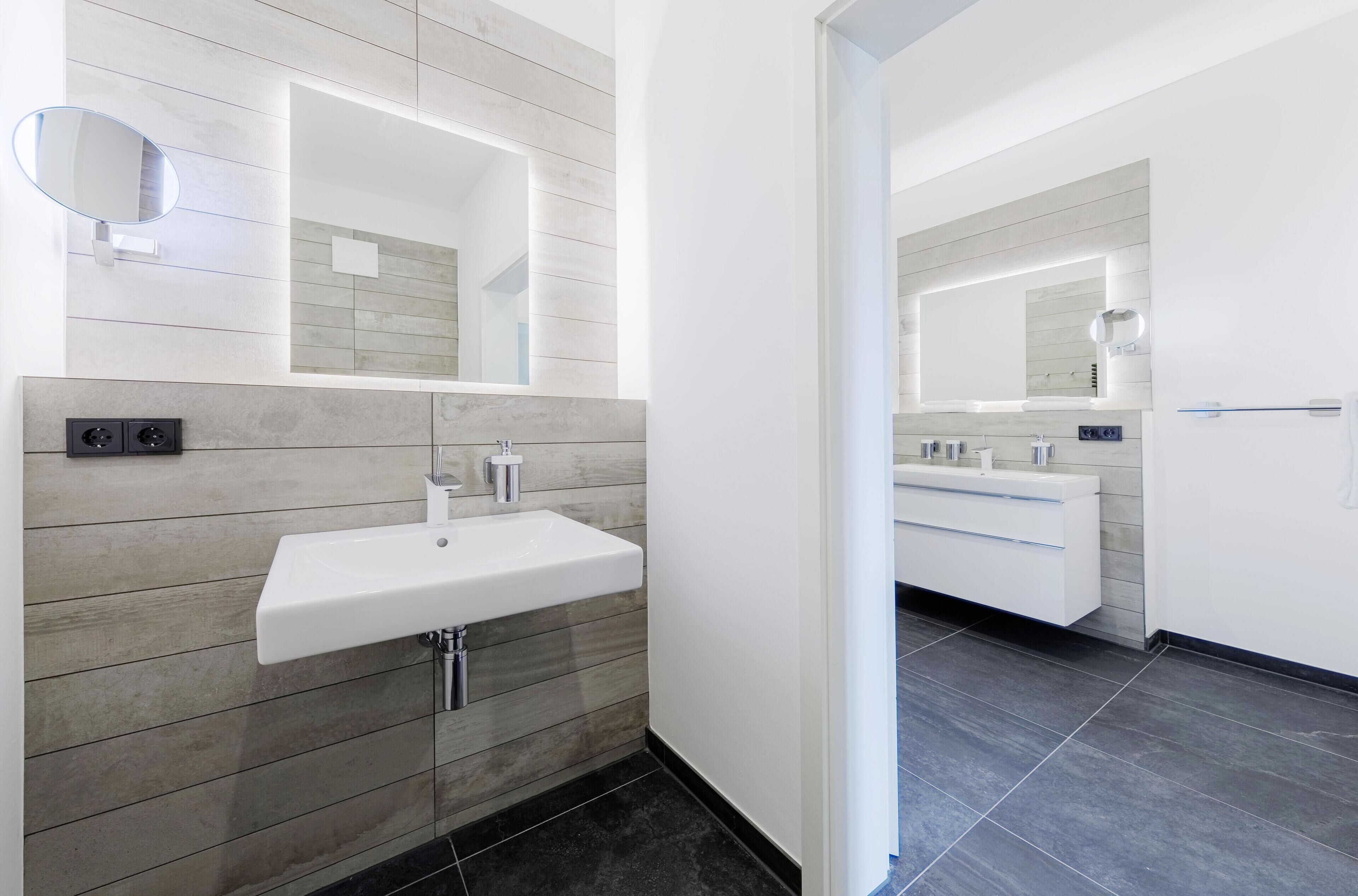 Une salle de bain moderne avec un lavabo blanc, un grand miroir et une coiffeuse avec un miroir.
