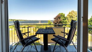 A balcony with a table and two chairs, overlooking a body of water and greenery. - Seeadler Vacation Rental – View of Lake Müritz from the Balcony (Waren (Müritz))