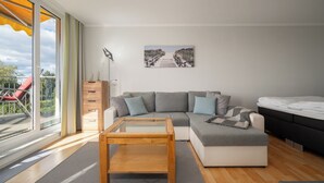 A modern living room with a glass coffee table, grey sofa, and a bed. - Vacation apartment "Seepferdchen" with a fantastic view of the Müritz (Waren (Müritz))