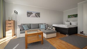 A modern, well-lit room with a sofa, ottoman, and a bed. There is a wooden coffee table and a grey rug. - Vacation apartment "Seepferdchen" with a fantastic view of the Müritz (Waren (Müritz))