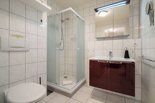 A modern bathroom with a glass-enclosed shower, a white toilet, and a vanity with a mirror.