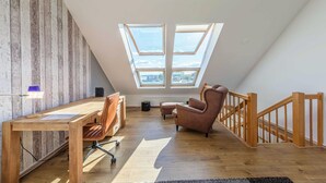 A modern loft bedroom with a sloped ceiling, skylights, a wooden desk, a chair, a sofa, and a staircase. - "Seeblick" Vacation Rental at the Marina with a View of Lake Müritz (Waren (Müritz))