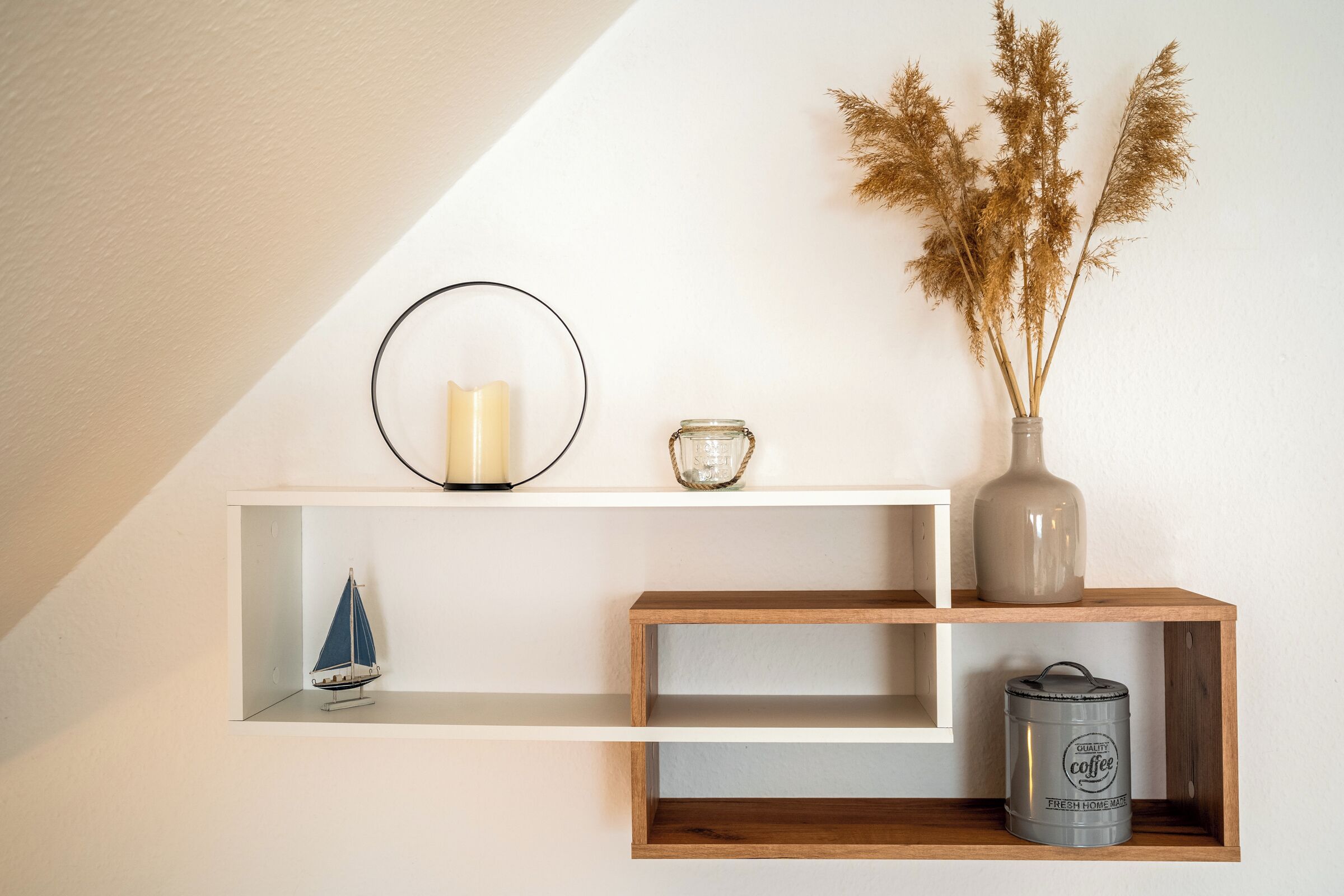A shelf with a candle, a vase with dried plants, a small sailboat, and a coffee can.