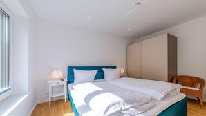 Ein modernes Schlafzimmer mit einem großen Bett, einem Nachttisch mit Lampe, einem Korbsessel und einem Kleiderschrank.