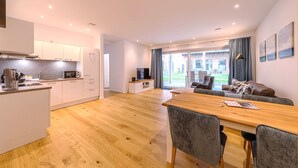 A modern kitchen with white cabinets, a wooden dining table, and a grey sofa in a bright living area with large windows. - "Inselpirat" Vacation Rental in the Island Town of Malchow (Malchow)