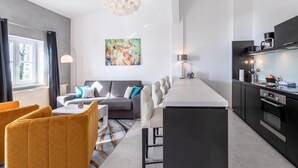 Een moderne woonkamer met een bank, een eettafel met stoelen, en een keukenhoek met een aanrecht en apparatuur.