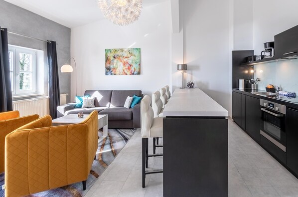 A modern living room with a sofa, a dining table with chairs, and a kitchen area with a countertop and appliances.