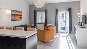 Un soggiorno moderno con un divano, un tavolino da caffè e due poltrone. Si nota un quadro appeso al muro, un lampadario e un televisore su un mobile.