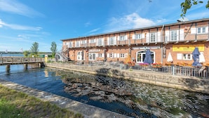 Un edificio lungo il fiume con posti a sedere all'aperto e un ponte sullo sfondo.