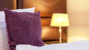 A neatly made bed with a purple textured pillow and a white pillow, a bedside lamp, and a headboard.