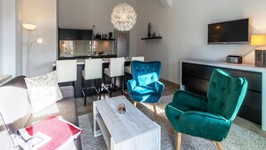 A modern living room with a sofa, two chairs, a coffee table, a TV, and a kitchen area in the background. - Vacation apartment "Kietz-Quartier" in the historic Kietzspeicher in Waren (Müritz) (Waren (Müritz))
