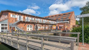 A wooden bridge over water leading to a brick building with multiple windows and balconies. - Vacation apartment "Kietz-Quartier" in the historic Kietzspeicher in Waren (Müritz) (Waren (Müritz))