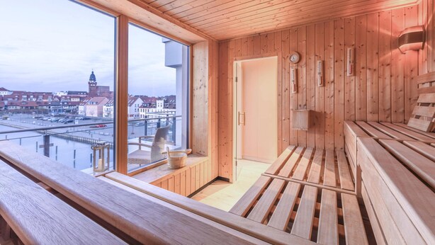 A wooden sauna with benches and a window overlooking a cityscape. - Vacation apartment "Kietz-Quartier" in the historic Kietzspeicher in Waren (Müritz) (Waren (Müritz))