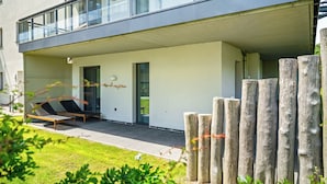 Un edificio moderno con techo plano, ventanas grandes y un espacio al aire libre cubierto con dos sillones.