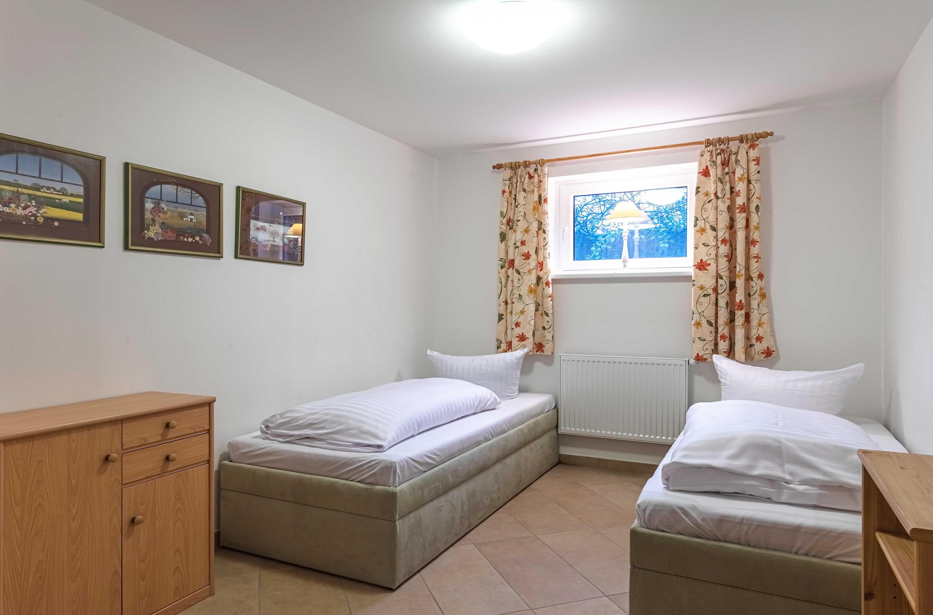 Un dormitorio con dos camas, un aparador de madera y una ventana con cortinas florales.