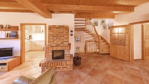 A spacious living area with a brick fireplace, wooden ceiling beams, a staircase, and a television. - "Havelquelle" Vacation Home in Kratzeburg, surrounded by beech forests and lakes (Kratzeburg)