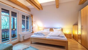 A bedroom with a wooden bed, a nightstand, a wardrobe, and large windows with a view of trees. - "Havelquelle" Vacation Home in Kratzeburg, surrounded by beech forests and lakes (Kratzeburg)